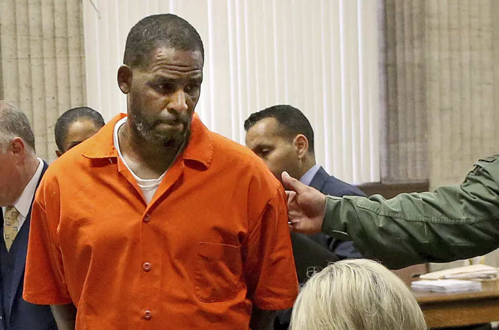 R. Kelly appears in a Chicago courtroom in 2019 wearing an orange prison jumpsuit. This image resurfaces as the U.S. Supreme Court declines to hear his final appeal, leaving his 30-year federal sentence intact. His legal team recently raised concerns about his safety behind bars, including allegations of a prison murder plot. (Photo: Antonio Perez / Chicago Tribune / Associated Press)