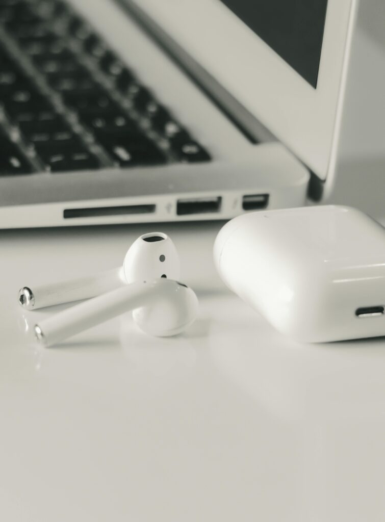 Apple AirPods and charging case on a desk next to a laptop keyboard